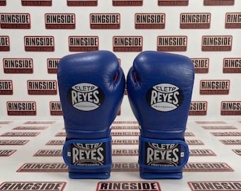 May include: A pair of blue boxing gloves with the brand name "Cleto Reyes" prominently displayed. The gloves have a sleek design with a wrist strap featuring the brand name. The background features the word "Ringside" repeated.