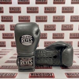 May include: A pair of gray leather boxing gloves with the brand name "CLETD REYES PROFESSIONAL" visible. The gloves are displayed on a background with the text "RINGSIDE PRESTIGE" repeated.