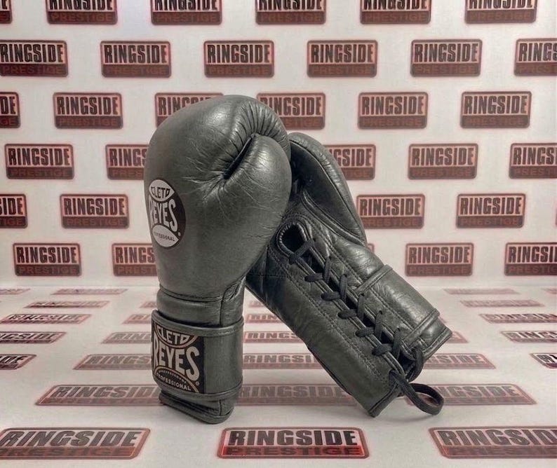 May include: A pair of gray leather boxing gloves with the brand name "CLETO REYES PROFESSIONAL" visible on the wrist strap and the glove. The gloves are laced up and appear to be new.