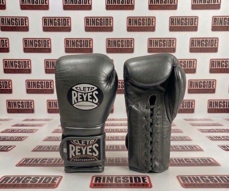 May include: A pair of gray leather boxing gloves. The gloves are laced up and feature the "CLETO REYES PROFESSIONAL" logo. The background has a repeating pattern of "RINGSIDE PRESTIGE" logos.
