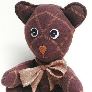 May include: A brown and tan plaid teddy bear with black button eyes and a brown nose. The bear is wearing a tan bow around its neck.