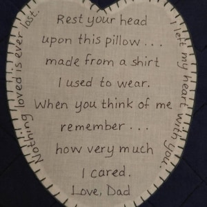 May include: A white heart-shaped pillow with a handwritten message that reads: "Rest your head upon this pillow... made from a shirt I used to wear. When you think of me remember... how very much I cared. Love, Dad."  The pillow is stitched with a dark blue thread.