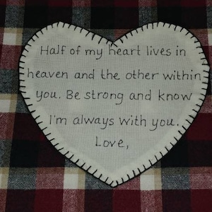 May include: A white heart-shaped fabric patch with black stitching around the edges. The patch has a message embroidered on it that reads: "Half of my heart lives in heaven and the other within you. Be strong and know I'm always with you. Love,"