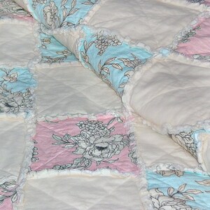 May include: A white, pink, and blue patchwork quilt with a floral pattern. The quilt is made of soft, comfortable fabric and has a ruffled edge.