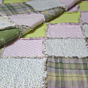 May include: A patchwork quilt with a variety of fabrics in shades of green, pink, and white. The quilt is made with a simple square pattern and has a frayed edge.