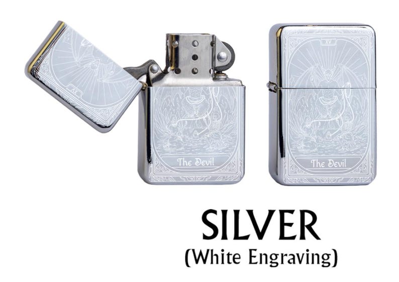 May include: Silver lighter with white engraving featuring a detailed illustration of The Devil tarot card. The lighter is shown open and closed, with the text "The Devil" at the bottom. The word "SILVER" is displayed below the lighters.