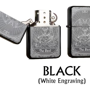 May include: Black metal lighter with white engraving featuring a tarot card design. The lighter is shown open and closed, with the text "The Devil" visible. The image also includes the word "BLACK" and "(White Engraving)".