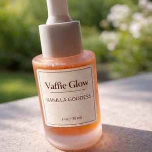 Op de afbeelding: Een kleine, matglazen fles met een druppelaar. De fles bevat een goudkleurige vloeistof en heeft een etiket met de tekst "Vaffie Glow VANILLA GODDESS 1 oz / 30 ml."
