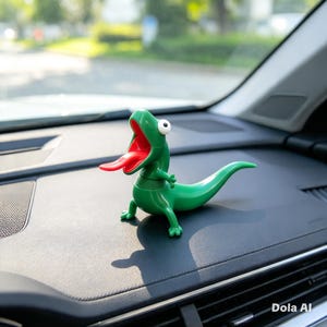 Puede incluir: Una figura de lagarto verde con la boca muy abierta, una lengua roja larga y un solo ojo blanco con pupila negra. La criatura tiene un acabado liso y brillante, un cuello segmentado y una cola larga sobre una superficie de salpicadero.