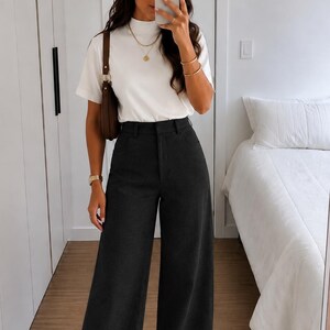 Peut inclure: Un haut blanc à manches courtes et col montant associé à un pantalon large gris anthracite à taille haute. La tenue comprend un sac à bandoulière marron, des colliers dorés superposés, des bracelets dorés, une montre dorée et des baskets blanches.