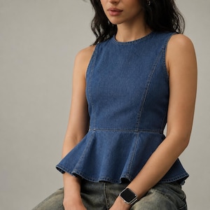 May include: A sleeveless blue denim peplum top featuring a round neckline, structured princess seams running vertically down the front, and a flared hemline that creates a distinct peplum silhouette. The fabric is a medium-wash blue denim.