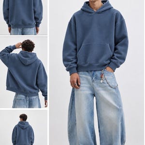 May include: A solid blue hooded sweatshirt with long sleeves, a front kangaroo pocket, and ribbed cuffs paired with light-wash, wide-leg denim jeans featuring a silver chain accessory attached to the waistband and white sneakers.