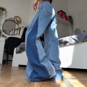 May include: Wide-leg denim jeans featuring a two-tone design with light blue panels on the front and back, contrasted by dark blue vertical panels running down the outer sides of each leg, complete with standard belt loops and pockets.