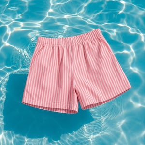Peut inclure: Un short à motif rayé vertical rose clair et blanc. Le vêtement est doté d'une taille élastique et d'une coupe décontractée, fabriqué dans un tissu léger adapté aux conditions météorologiques chaudes et ensoleillées.
