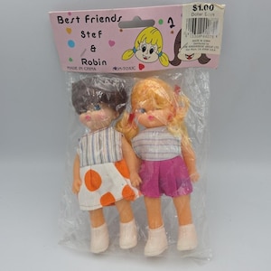 May include: Two vintage doll figures, Stef and Robin, in a plastic package. Stef wears a white dress with orange polka dots, and Robin wears a pink skirt. The package reads "Best Friends" and "$1.00 Dollar Doves."