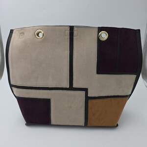 May include: A geometric-patterned tote bag with a mix of neutral colors, including beige, brown, and burgundy. The bag features black trim and gold-colored eyelets. The bag's design is modern and stylish.