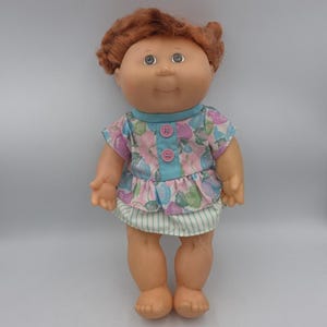 Könnte beinhalten: Handgefertigtes Holzschild mit dem Wort "Welcome" in verspielter Schrift. Es hat einen weißen, abgenutzten Hintergrund und einen dunkelbraunen Rahmen, ideal für eine Eingangstür. Das Schild ist etwa 30 cm breit und 15 cm hoch.