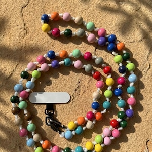 Könnte beinhalten: Eine farbenfrohe Handy-Kette mit bunten Perlen in Pink, Blau, Grün und Orange. Die runden Perlen sind auf einer weißen Schnur aufgefädelt und mit einem schwarzen Verschluss versehen.