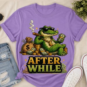 Könnte beinhalten: Ein lila T-Shirt mit einem Cartoon-Alligator, der eine Sonnenbrille, eine goldene Kette trägt und Geld und eine Zigarre hält. Der Text "AFTER WHILE" wird in Gold und Grün angezeigt.