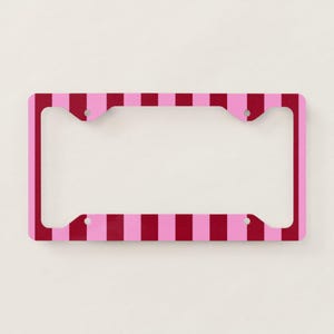 May include: A rectangular license plate frame featuring a repeating vertical striped pattern in alternating shades of dark red and light pink. The frame has four circular mounting holes positioned at the top and bottom corners for attachment.