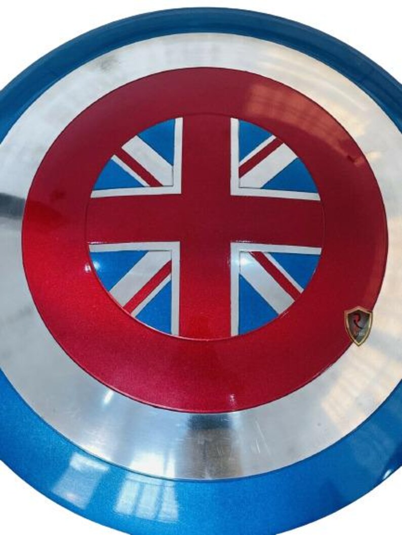 May include: A round shield with a red center featuring a Union Jack design, surrounded by a silver band and a blue outer rim. A small emblem is on the lower right. The shield is a prop or collectible.