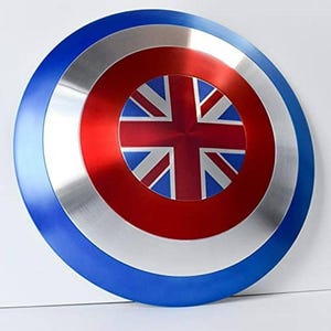 May include: A round shield with a blue, silver, and red color scheme. The center features a red circle with a Union Jack design. The outer edge is blue, with a silver band in the middle. A patriotic themed item.