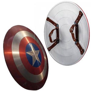 K&ouml;nnte beinhalten: Zwei Captain America Schilde. Ein Schild ist angewinkelt und zeigt ein rotes, silbernes und blaues Design mit einem Stern. Das andere Schild zeigt die R&uuml;ckseite mit braunen Lederriemen und einer wei&szlig;en Oberfl&auml;che.