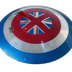 May include: A round, metallic shield with a blue, silver, and red color scheme. The center features a red circle with a Union Jack design. A small emblem is visible on the left side. The shield is a prop or collectible.
