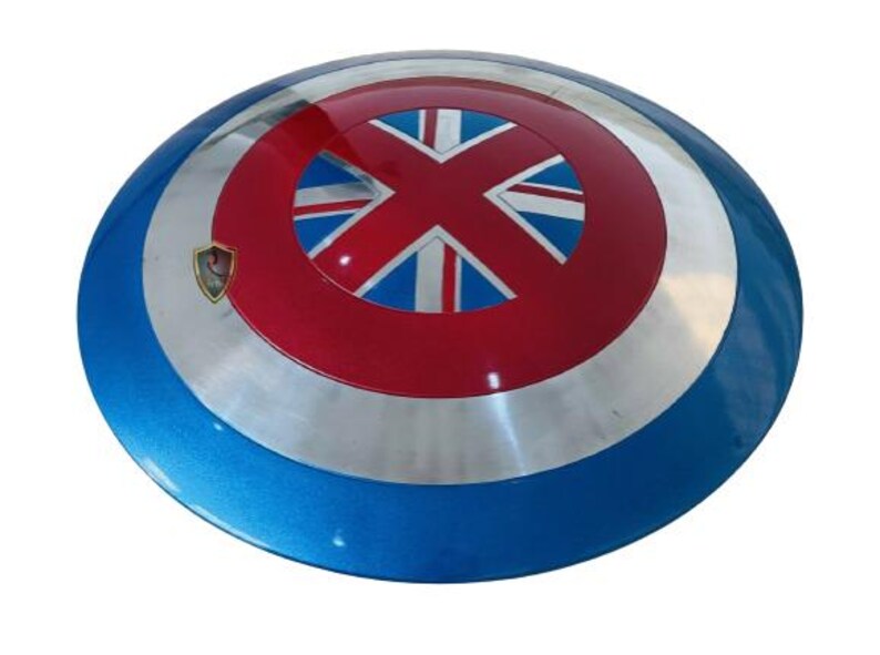 May include: A round, metallic shield with a blue, silver, and red color scheme. The center features a red circle with a Union Jack design. A small emblem is visible on the left side. The shield is a prop or collectible.