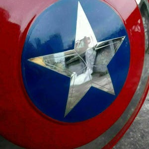 K&ouml;nnte beinhalten: Ein rot, wei&szlig; und blaues Schild mit einem gro&szlig;en silbernen Stern in der Mitte. Das Schild hat ein kreisf&ouml;rmiges Design mit einem blauen Kreis in der Mitte und einem silbernen Band am Rand.