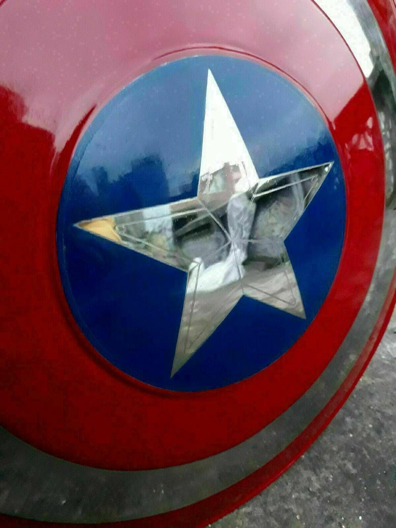 K&ouml;nnte beinhalten: Ein rot, wei&szlig; und blaues Schild mit einem gro&szlig;en silbernen Stern in der Mitte. Das Schild hat ein kreisf&ouml;rmiges Design mit einem blauen Kreis in der Mitte und einem silbernen Band am Rand.