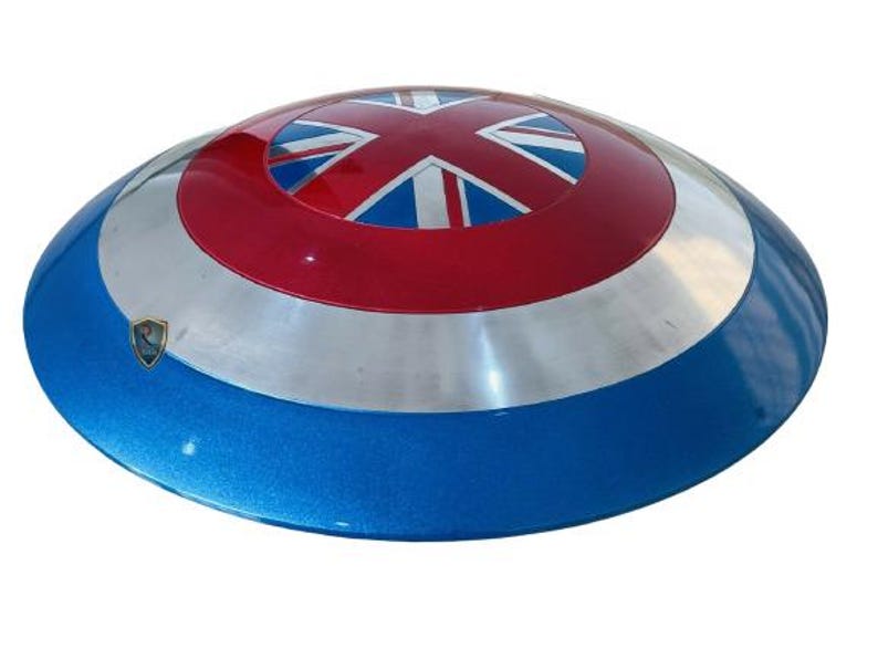 May include: A round shield with a blue, silver, and red color scheme. The shield features a Union Jack design in the center, with a silver band and a blue outer rim. A small emblem is visible on the shield's surface.