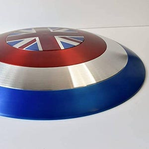 May include: A round shield with a Union Jack design in the center. The shield has a red, silver, and blue color scheme. The outer edge is blue, followed by a silver band, and a red center with the Union Jack.