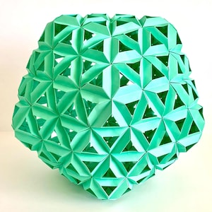 May include: A mint green, geometric paper sculpture. The spherical form is constructed from numerous folded triangular and star-shaped paper elements, creating a complex, openwork design. The sculpture is displayed against a white background.