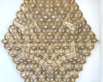 May include: A gold-colored, geometric wall art piece with a honeycomb-like design. The artwork is composed of interconnected, three-dimensional cube shapes, creating a textured surface. The piece is mounted on a white wall, showcasing its intricate pattern.