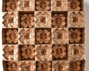 May include: A square, geometric wall art piece composed of 25 individual square cells. Each cell features a complex, repeating pattern in shades of bronze and gold. The overall design is symmetrical and creates a textured, three-dimensional effect.