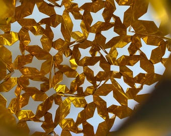 May include: A gold-colored metallic structure featuring a repeating geometric pattern of interconnected four-pointed stars and diamond shapes. The surface of the material has a crinkled, reflective texture that creates highlights and shadows.