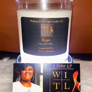 Può includere: Un portacandele in vetro trasparente con una candela bianca. La candela ha un'etichetta nera con il testo "Hope" e "Lily of the Valley". La candela è di 240 grammi. Due biglietti da visita sono davanti alla candela.