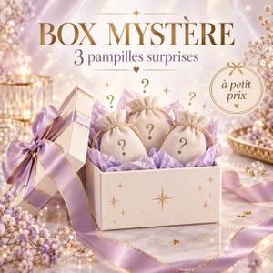 Peut inclure: Une boîte cadeau crème avec un ruban lavande, contenant trois petits pochons en tissu marqués d'un point d'interrogation. La boîte présente des étoiles dorées et le texte "BOX MYSTÈRE 3 pampilles surprises" et "à petit prix" dans un médaillon.