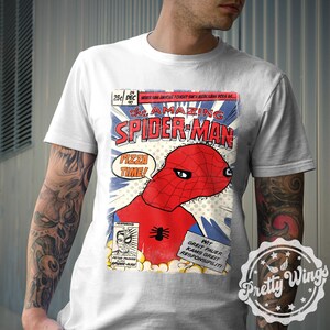May include: White t-shirt featuring a comic book-style graphic of Spider-Man with the text "PIZZA TIME!". The design includes the words "THE AMAZING SPIDER-MAN" and other text in a comic book layout. The shirt has a crew neck.