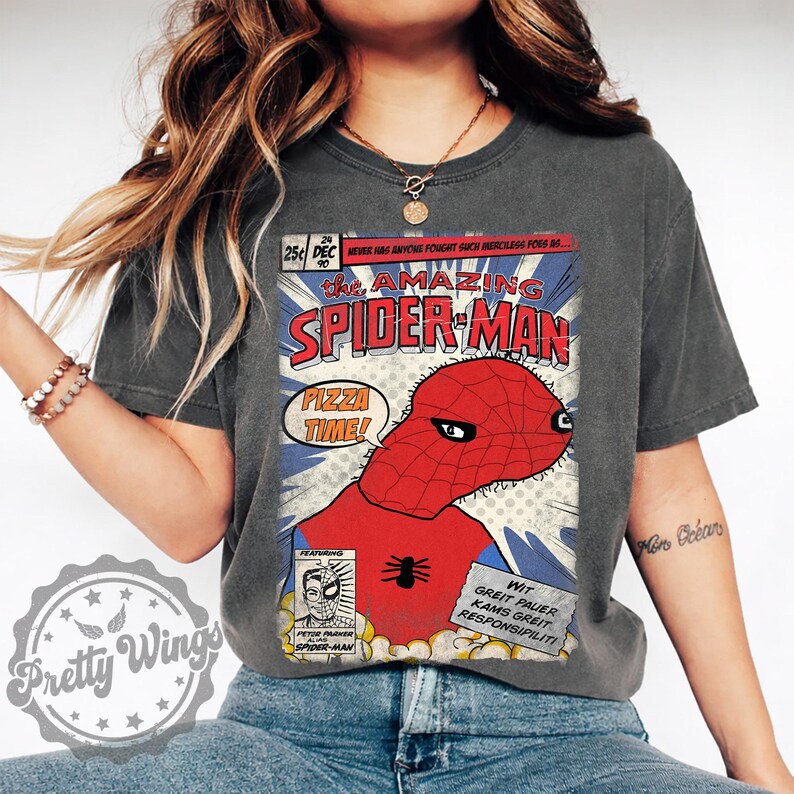 May include: Dark gray t-shirt featuring a comic book-style graphic of Spider-Man with the text "PIZZA TIME!". The graphic includes the words "The Amazing Spider-Man" and other comic book elements. The shirt is worn by a person.