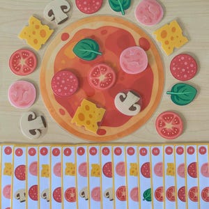 May include: A circular pizza game board with various topping pieces including pepperoni, mushrooms, cheese, tomatoes, and spinach. Below the pizza are seventeen rectangular cards numbered 3 through 19, each displaying a sequence of pizza toppings.