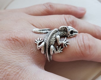 Puede incluir: Un anillo de plata con forma de lagarto con detalles negros. El anillo se lleva en un dedo.