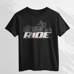 Puede incluir: Camiseta negra con un dibujo lineal blanco de una motocicleta. La palabra "RIDE" está impresa en blanco desgastado con líneas de acento naranja y gris. El diseño está centrado en la parte delantera de la camiseta.