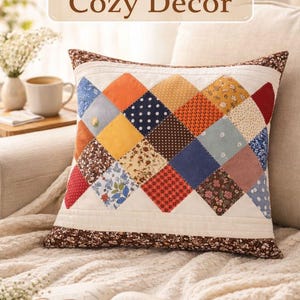 May include: A handmade, square cushion with a patchwork design featuring various fabrics in orange, blue, yellow, and floral patterns. The cushion has a brown floral border and the text "Handmade Cozy Decor" at the top.