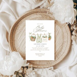 a baby shower invitation with a wicker basket and white flowers as the background.