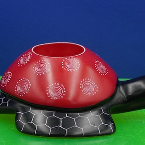 May include: A turtle-shaped decorative bowl featuring a smooth red shell with white spiral patterns. The head, tail, and flippers are black with a white hexagonal grid design etched onto the flippers. The turtle has a small white eye detail.