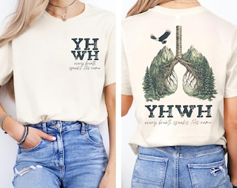 Könnte beinhalten: Cremefarbenes T-Shirt mit dem Text "YHWH" und "every breath speaks His name" auf der Vorderseite. Die Rückseite zeigt eine Grafik von Lungen, die aus Bergen und Bäumen gebildet werden, mit einem Adler und demselben Text.