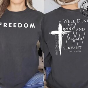 Puede incluir: Camiseta de manga larga gris oscuro con la palabra "FREEDOM" impresa en blanco en la parte delantera. La parte trasera presenta una cruz blanca y el texto "WELL DONE, MY good AND faithful SERVANT" con una referencia bíblica.