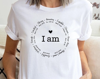 Könnte beinhalten: Weißes T-Shirt mit einem kreisförmigen Design mit den Worten "I am" in fetter Schrift, darüber ein kleines Herz. Der Kreis um den Text enthält Wörter wie "Amazing", "Capable" und "Beautiful".